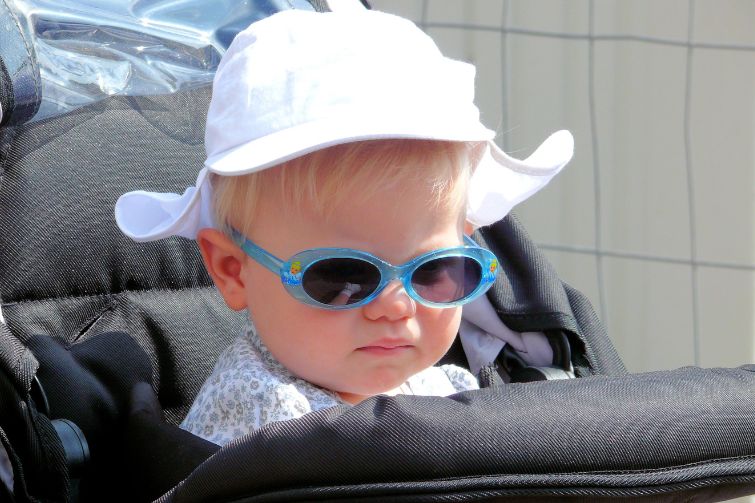 Toddler in pram with sunglasses and hat on.