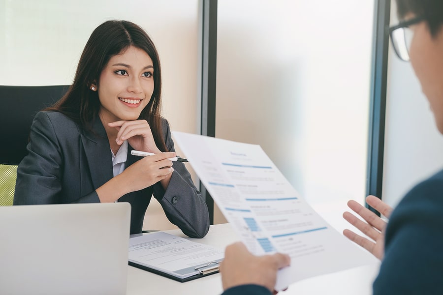 Lady in business suit sitting across the desk from someone reading her CV / resume
