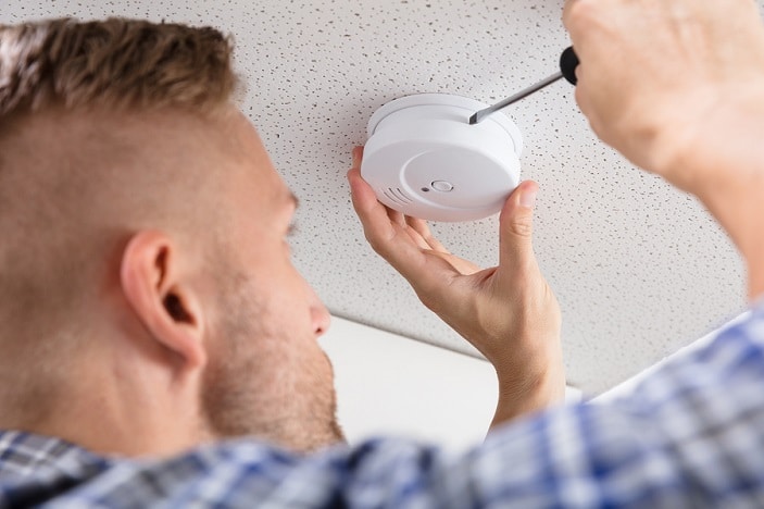 Close-up Of A Person's Hand Using Screwdriver To Install Smoke Detector On Ceiling At Home