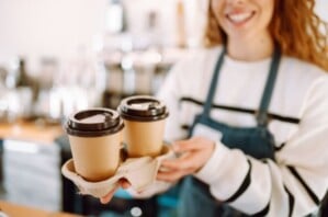 A lady holding two takeaway coffees in a try.