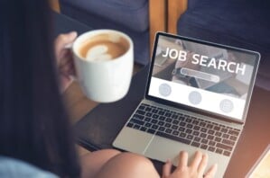 A person holding a cup of coffee in front of a computer screen, with job search on the display.
