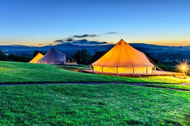 Several glamping tents at sunset with hills in background.