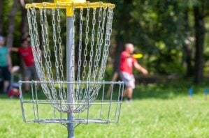 A player throwing a disc toward the disc golf basket.