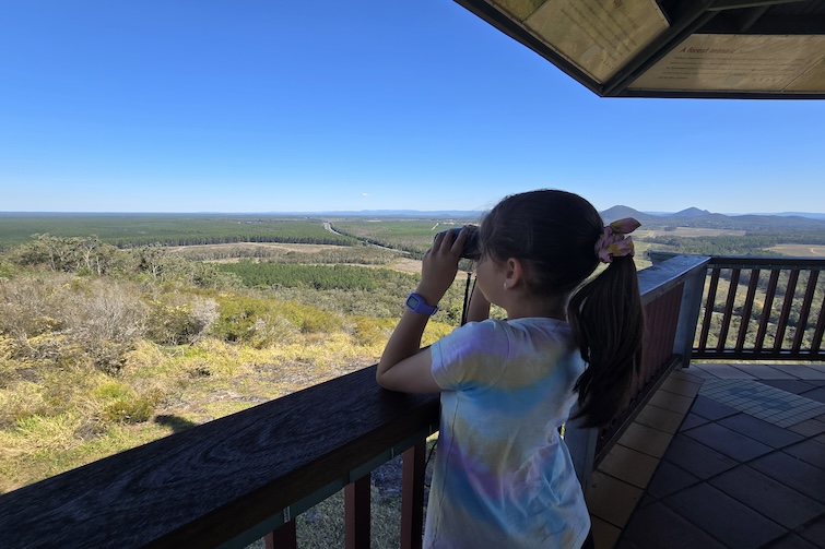 Girl looking out with binoculars from Wild Horse Mountain Lookout.