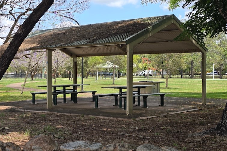 Covered picnic shelter outside fenced playground at Milton Park.