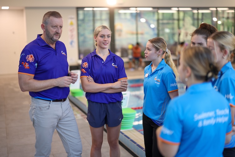 A group of people standing next to a pool at Carlile Swim.