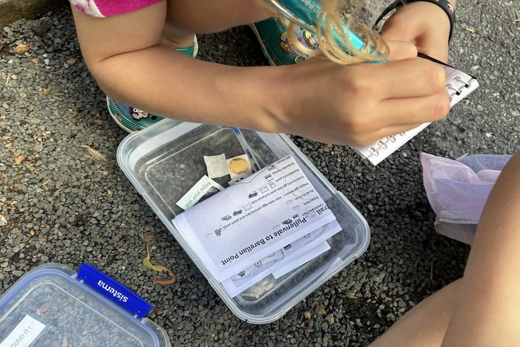 Children writing in a logbook at a geocaching location.