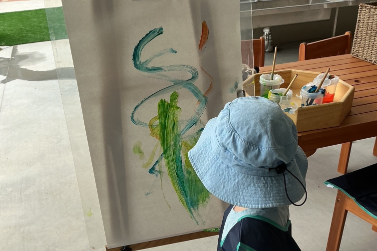 Corymbia Early Learning child painting on easel outdoors.