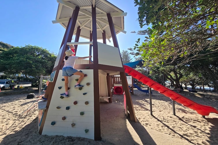 Wooden lighthouse play structure with a child climbing it at Happy Valley Playground in Caloundra.
