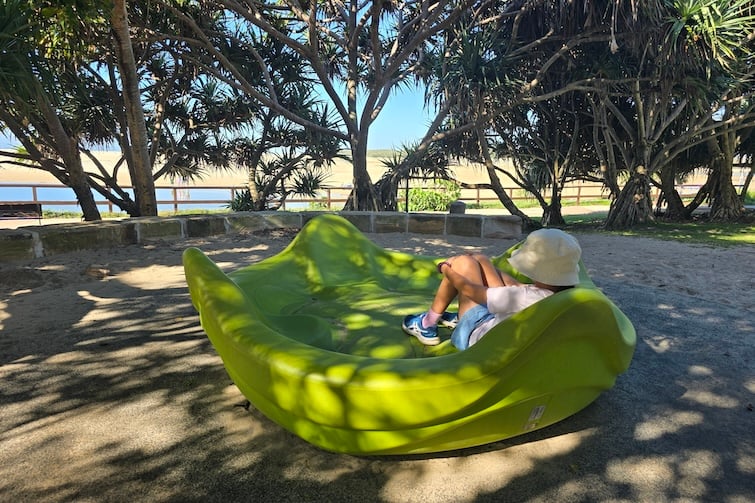Girl sitting on the green seated carousel at Happy Valley Playground in Caloundra.