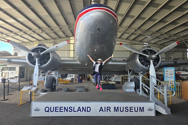 Child jumping in front of a plane and sign at Queensland Air Museum, Caloundra.